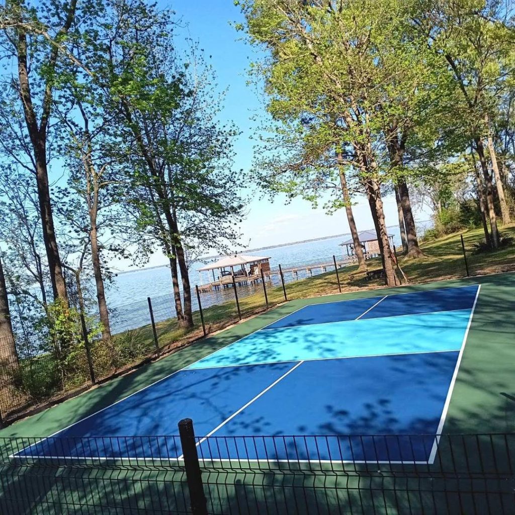 A lakeside pickleball court in Coldspring, Texas featuring shades of blue, transformed from a taped slab into a pro-level surface in just 3 days.