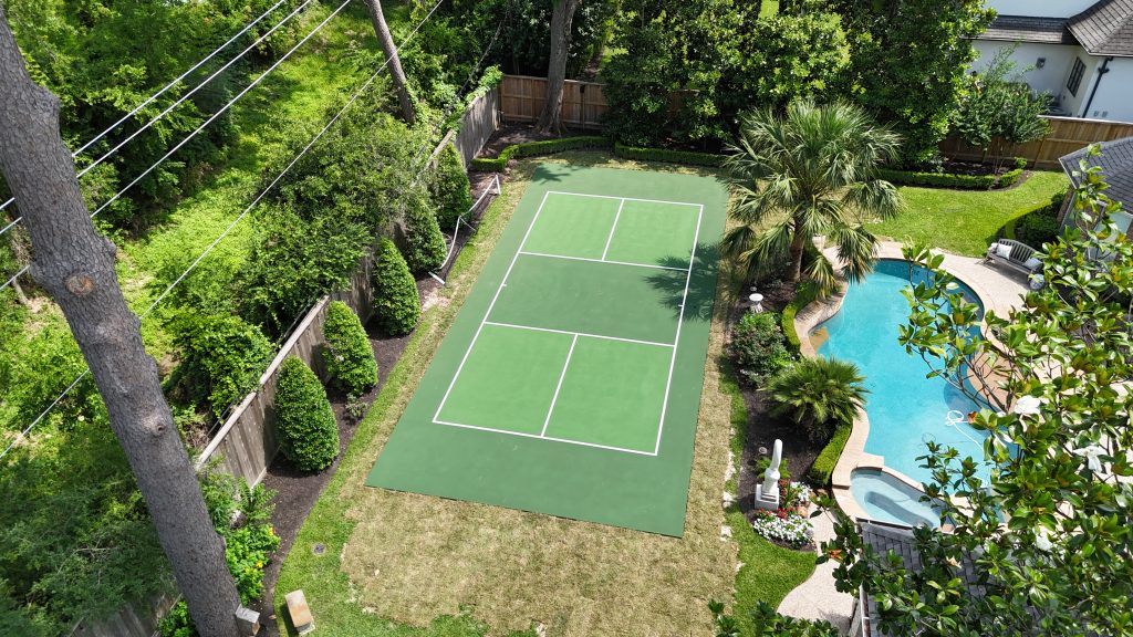 A pickleball court in Houston, Texas, featuring a green-on-green color scheme with medium green playing surface and tournament green surrounding areas. The court measures 60 by 26 feet.