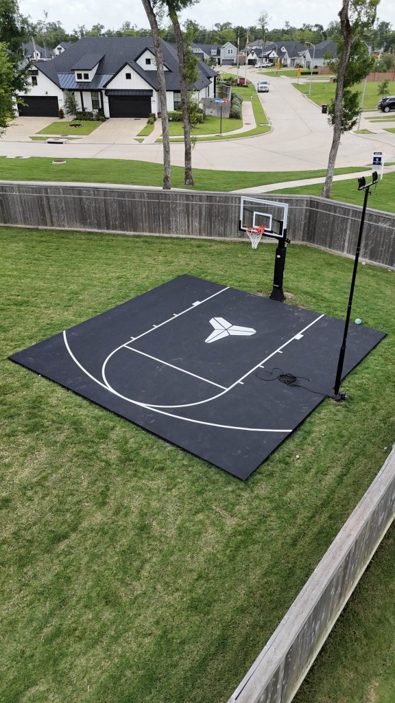 Backyard basketball court in Sienna, Texas featuring a custom Kobe logo, pro Ryval hoop, court lighting, and premium acrylic surfacing.