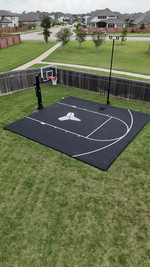 Backyard basketball court with painted three-point line, pro-grade Ryval hoop, custom color surface, and court lighting built for training at home.