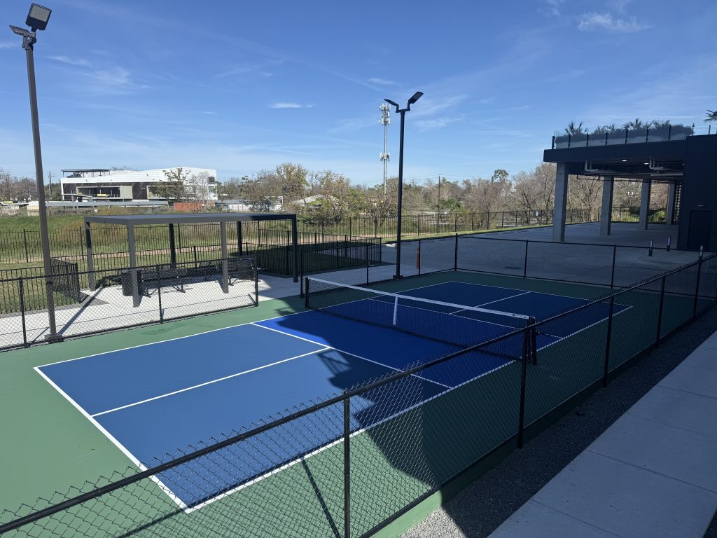 Side angle of blue commercial pickleball facility with green surround and black fencing.