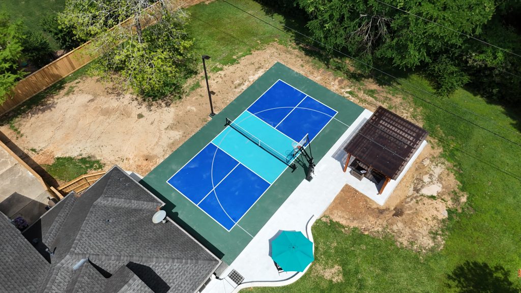 Aerial view of multi sport court with pickleball and basketball setup in residential backyard